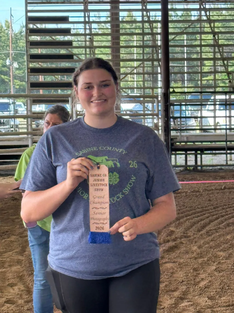 A graduating Sabine County senior exhibitor holding a Senior division ribbon, arena behind
